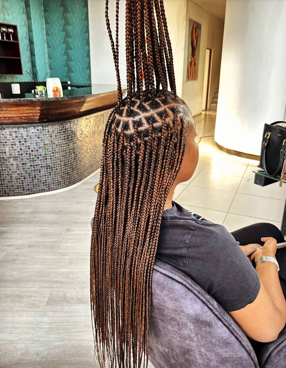 Client seated in the salon with long brown box braids and triangle parts